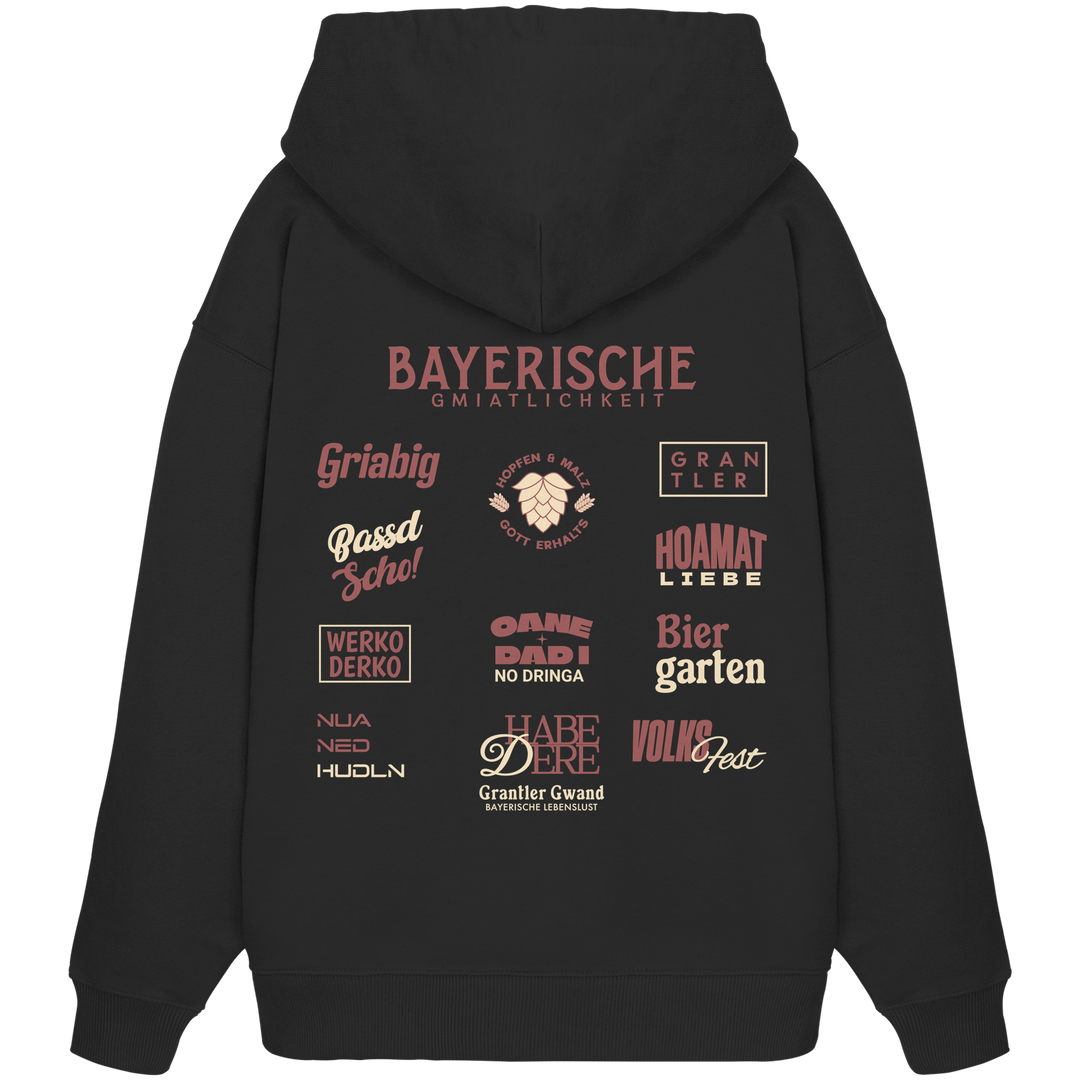 Schwarzer Oversize-Hoodie mit großem rotem Backprint „Bayerische Gmiatlichkeit“ und typischen bayerischen Begriffen wie Hoamatliebe, Biergarten, Volksfest, Grantler, Hopfen &amp; Malz und Griabig. Unisex Premium-Hoodie aus Bio-Baumwolle im modernen Streetwear-Style. Designed und bedruckt in Bayern von Grantler Gwand.