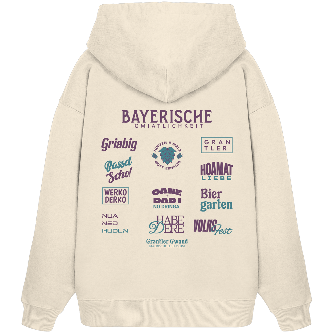 Beiger Oversize Hoodie mit großem lila Backprint „Bayerische Gmiatlichkeit“ und bayerischen Begriffen wie Hoamatliebe, Biergarten, Volksfest, Grantler, Hopfen &amp; Malz und Griabig. Unisex Premium-Hoodie aus Bio-Baumwolle im modernen Streetwear-Style. Designed und bedruckt in Bayern von Grantler Gwand.