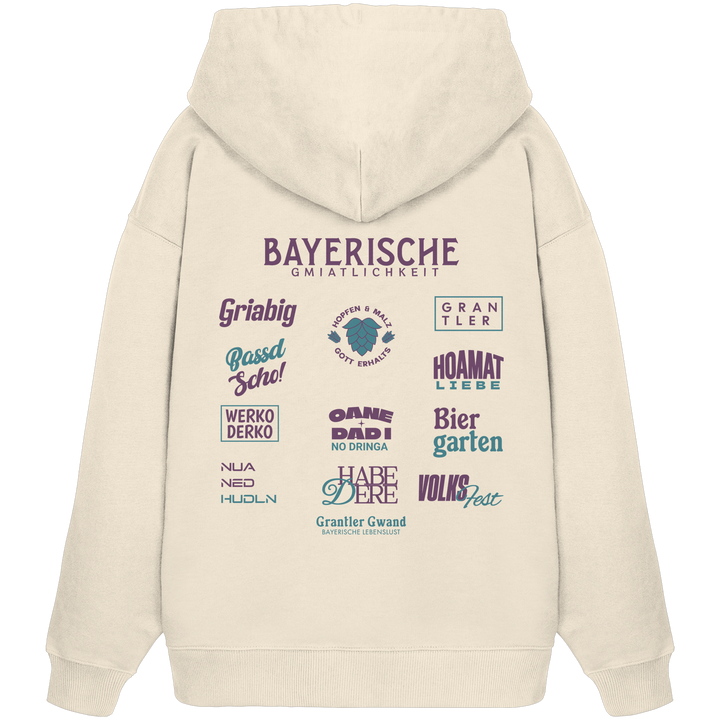 Beiger Oversize Hoodie mit großem lila Backprint „Bayerische Gmiatlichkeit“ und bayerischen Begriffen wie Hoamatliebe, Biergarten, Volksfest, Grantler, Hopfen &amp; Malz und Griabig. Unisex Premium-Hoodie aus Bio-Baumwolle im modernen Streetwear-Style. Designed und bedruckt in Bayern von Grantler Gwand.