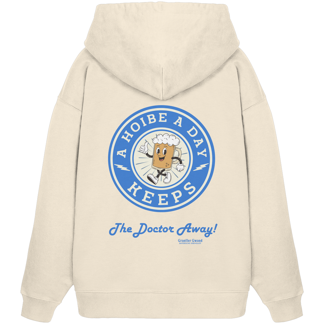 Beiger Oversize-Hoodie mit großem Backprint „A Hoibe A Day – Keeps the Doctor Away“ im Retro-Bierdeckel-Design mit blauen Akzenten. Extra schwerer Premium-Hoodie aus Bio-Baumwolle für Biergarten, Volksfest und bayerische Streetwear. Designed und bedruckt in Bayern von Grantler Gwand.