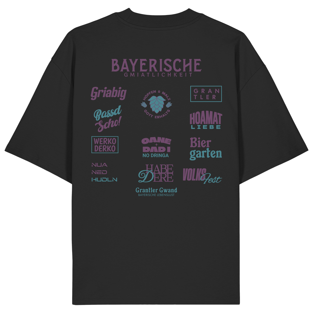 Schwarzes Oversize-Shirt mit großem lila Backprint „Bayerische Gmiatlichkeit“ und typischen bayerischen Begriffen wie Hoamatliebe, Biergarten, Volksfest, Grantler, Hopfen &amp; Malz und Griabig. Unisex Premium-Shirt aus Bio-Baumwolle im modernen Streetwear-Style. Designed und bedruckt in Bayern von Grantler Gwand.