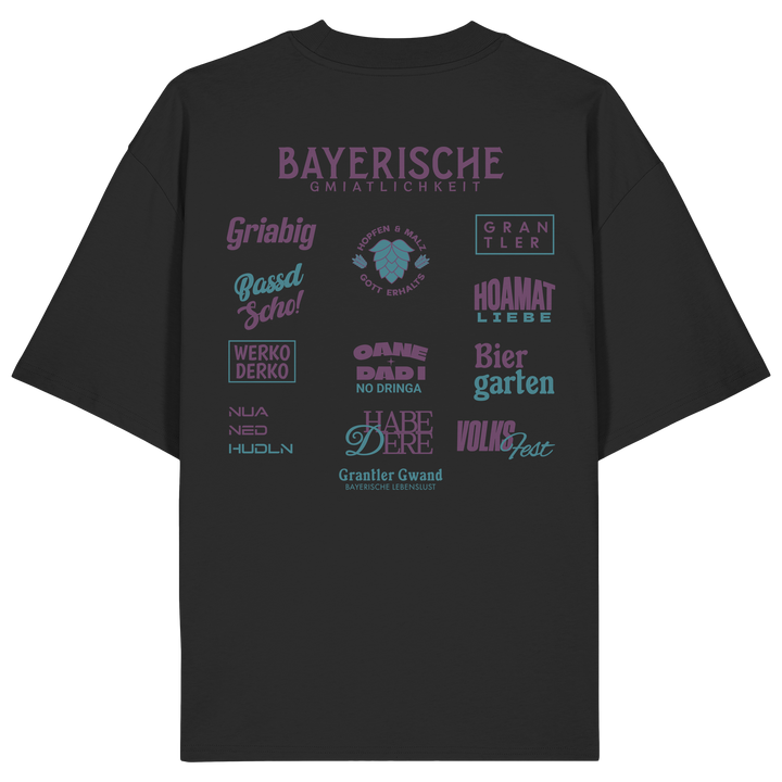 Schwarzes Oversize-Shirt mit großem lila Backprint „Bayerische Gmiatlichkeit“ und typischen bayerischen Begriffen wie Hoamatliebe, Biergarten, Volksfest, Grantler, Hopfen &amp; Malz und Griabig. Unisex Premium-Shirt aus Bio-Baumwolle im modernen Streetwear-Style. Designed und bedruckt in Bayern von Grantler Gwand.