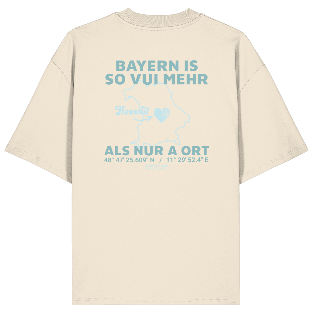 Cremefarbenes Oversize T-Shirt von Grantler Gwand mit grünem Backprint „Bayern is so vui mehr als nur a Ort“ und Bayern-Silhouette – bayerisches Streetwear Shirt aus Bio-Baumwolle.