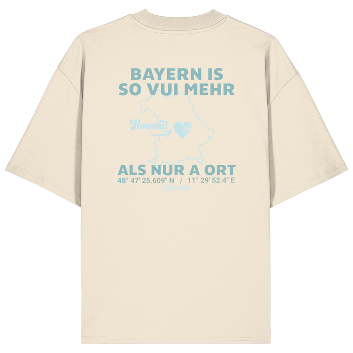 Cremefarbenes Oversize T-Shirt von Grantler Gwand mit grünem Backprint „Bayern is so vui mehr als nur a Ort“ und Bayern-Silhouette – bayerisches Streetwear Shirt aus Bio-Baumwolle.