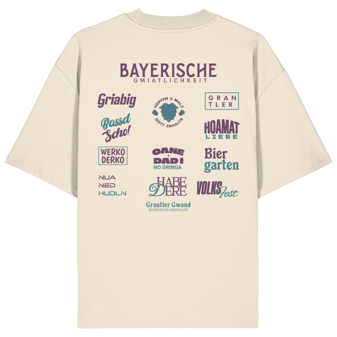 Beiges Oversize-Shirt mit großem lila Backprint „Bayerische Gmiatlichkeit“ und typischen bayerischen Begriffen wie Hoamatliebe, Biergarten, Volksfest, Grantler, Hopfen &amp; Malz und Griabig. Unisex Premium-Shirt aus Bio-Baumwolle im modernen Streetwear-Style. Designed und bedruckt in Bayern von Grantler Gwand.
