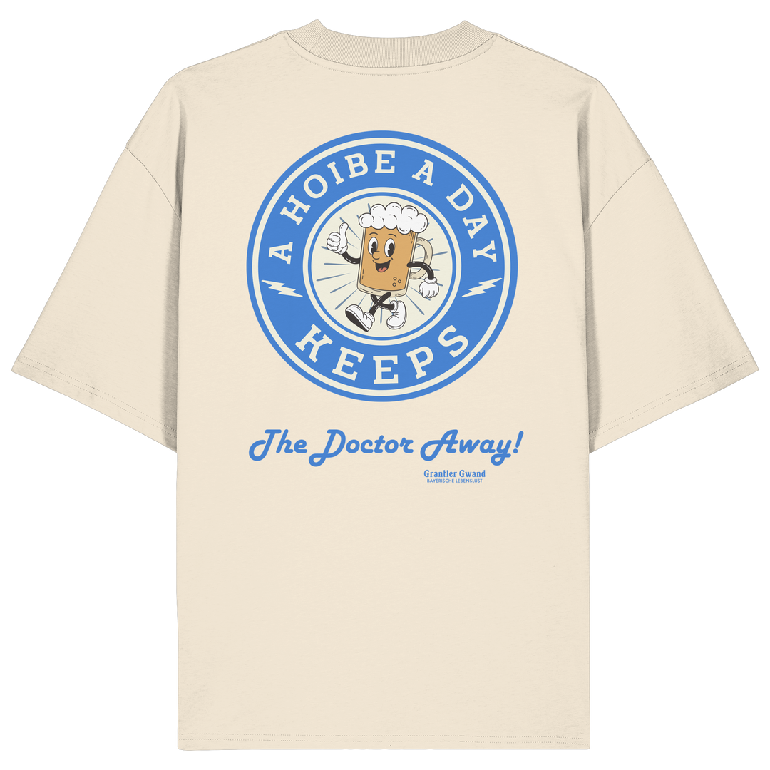 Oversize Unisex-Shirt in Beige mit großem Backprint „A Hoibe A Day – Keeps the Doctor Away“ im Retro-Bierdeckel-Design mit blauen Akzenten. Modernes bayerisches Streetwear-Shirt für Biergarten, Volksfest und gesellige Momente. Designed und bedruckt in Bayern von Grantler Gwand.