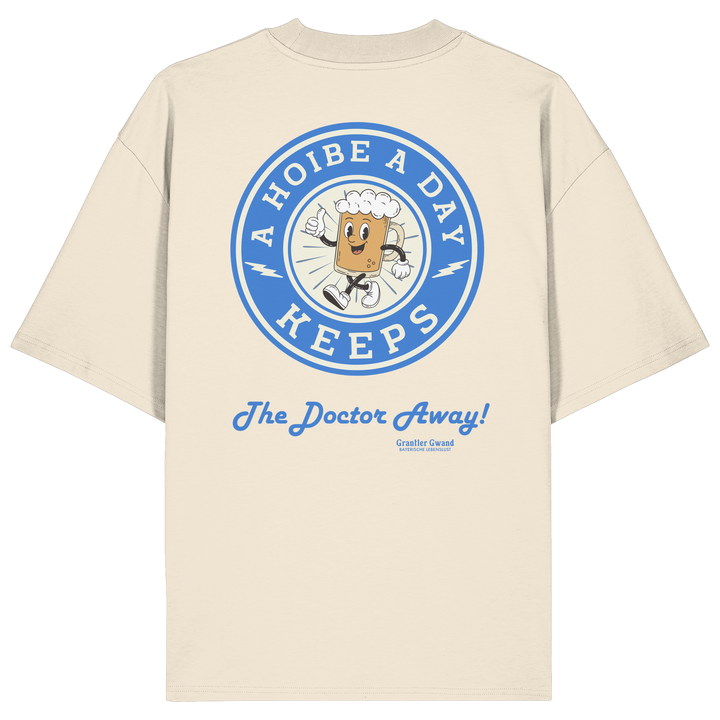 Oversize Unisex-Shirt in Beige mit großem Backprint „A Hoibe A Day – Keeps the Doctor Away“ im Retro-Bierdeckel-Design mit blauen Akzenten. Modernes bayerisches Streetwear-Shirt für Biergarten, Volksfest und gesellige Momente. Designed und bedruckt in Bayern von Grantler Gwand.