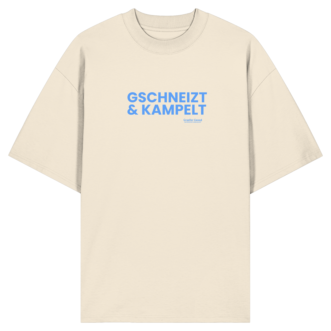 Beiges Oversize-T-Shirt mit blauem Frontprint „Gschneizt &amp; Kampelt“. Modernes bayerisches Streetwear-Shirt mit Dialekt-Motiv für Volksfest, Biergarten und Alltag. Hochwertige Bio-Baumwolle, designed und bedruckt in Bayern von Grantler Gwand.