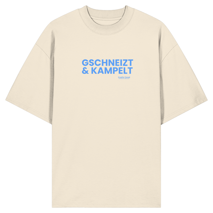 Beiges Oversize-T-Shirt mit blauem Frontprint „Gschneizt &amp; Kampelt“. Modernes bayerisches Streetwear-Shirt mit Dialekt-Motiv für Volksfest, Biergarten und Alltag. Hochwertige Bio-Baumwolle, designed und bedruckt in Bayern von Grantler Gwand.