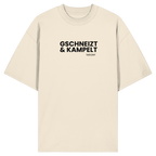 Beiges Oversize-T-Shirt mit schwarzem Frontprint „Gschneizt & Kampelt“. Modernes Unisex-Shirt mit bayerischem Dialekt im minimalistischen Streetwear-Design für Volksfest, Biergarten und Alltag. Hochwertige Bio-Baumwolle, designed und bedruckt in Bayern von Grantler Gwand.